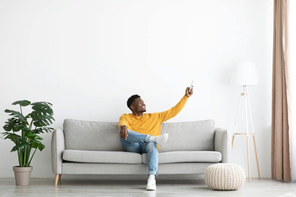 Relaxed african american guy sitting on couch, turning on AC